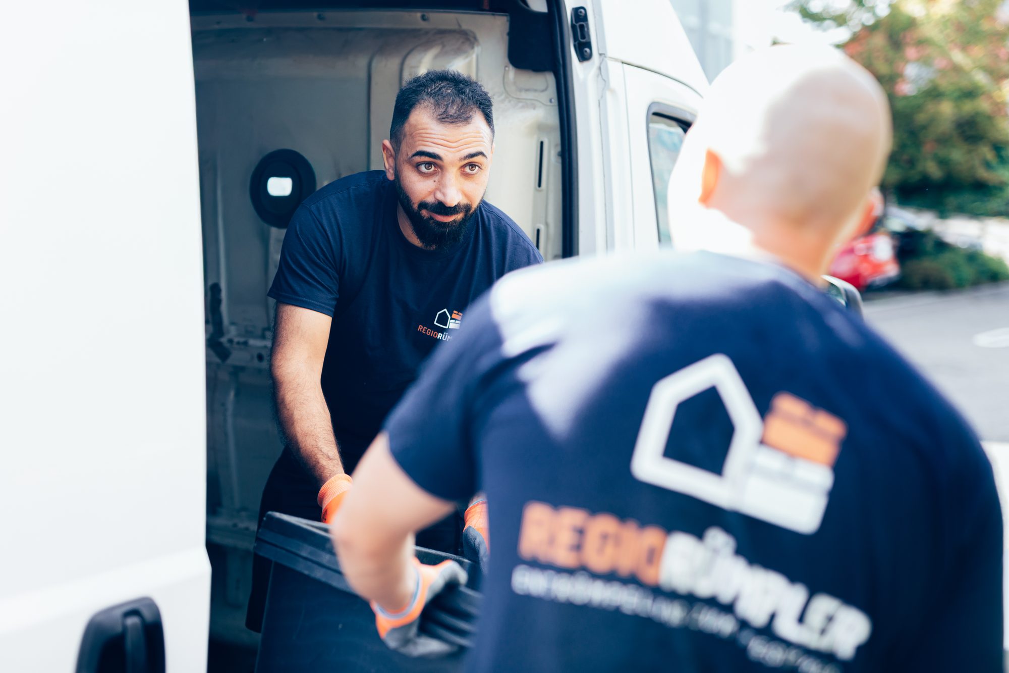 Ein Mitarbeiter lädt eine Kiste in den Transporter, der den Hausrat zur Entsorgung fährt.