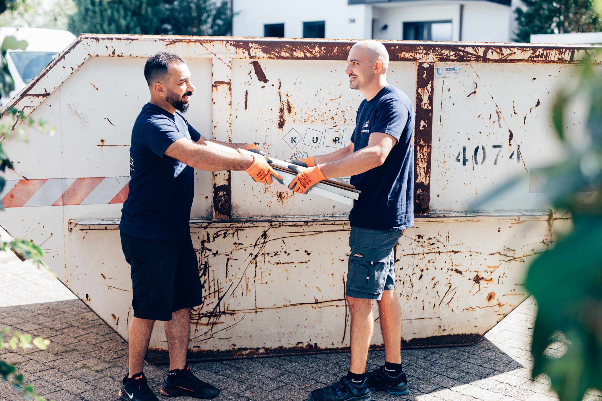 Zwei Mitarbeiter von RegioRümpler reichen sich am Container ein ausgebautes Metallrohr.