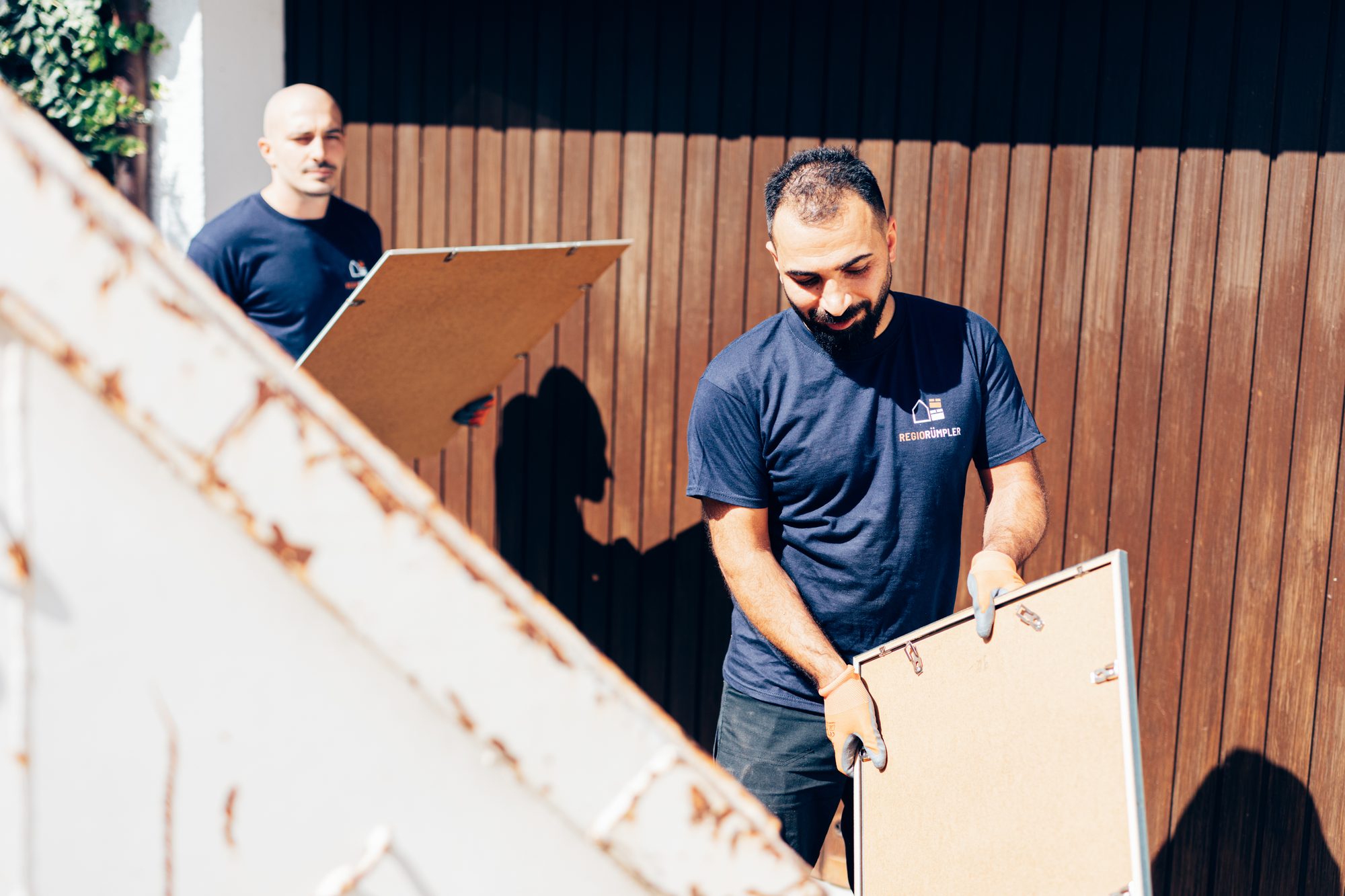 Zwei Mitarbeiter bringen bei einer Entrümpelung alte Bilderrahmen zum Container.