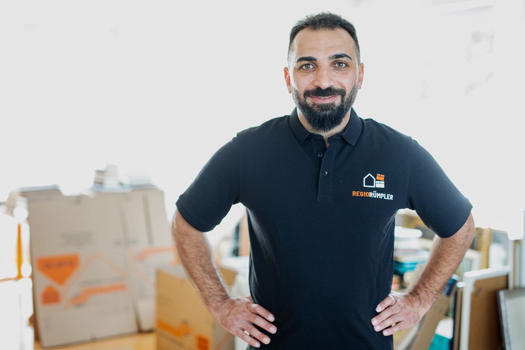 Ramazan Özdemir, Inhaber von RegioRümpler, im schwarzen Firmenpolo vor Umzugskartons.