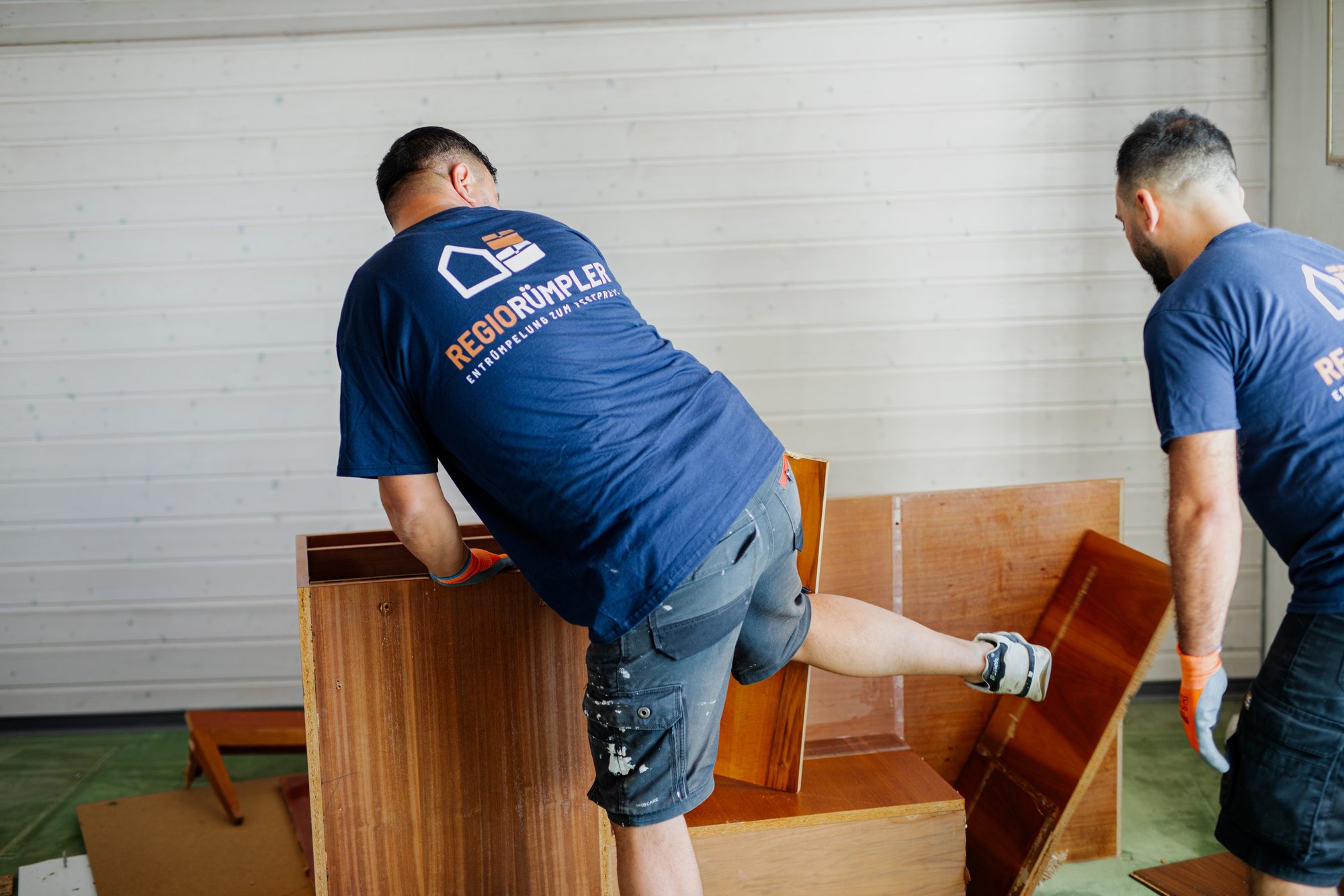 Zwei Mitarbeiter zerlegen beim Rückbau einen Holzschrank im Dachzimmer.