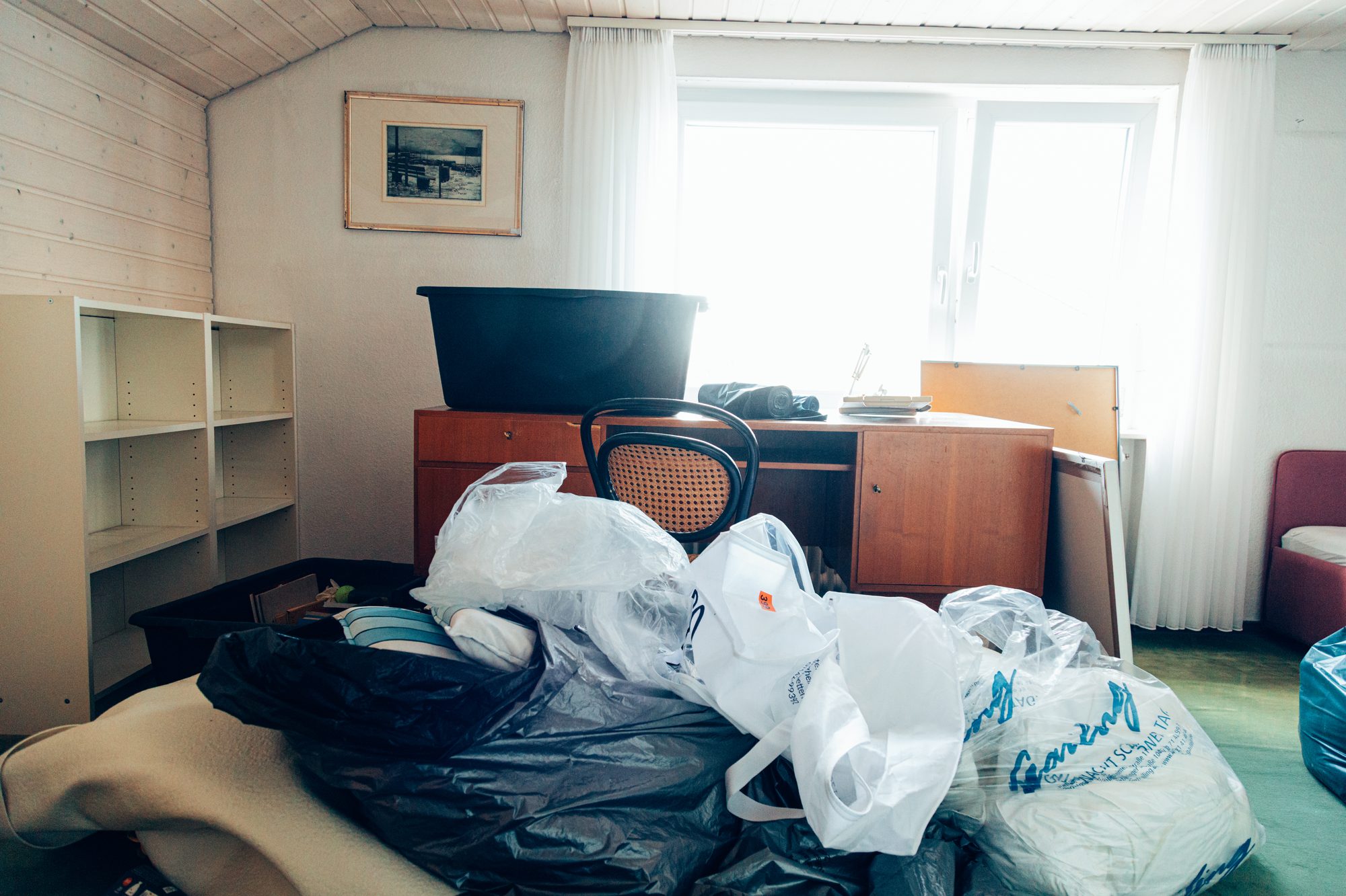 Müllsäcke vor Schreibtisch und Regal in einem Dachzimmer vor der Wohnungsentrümpelung.