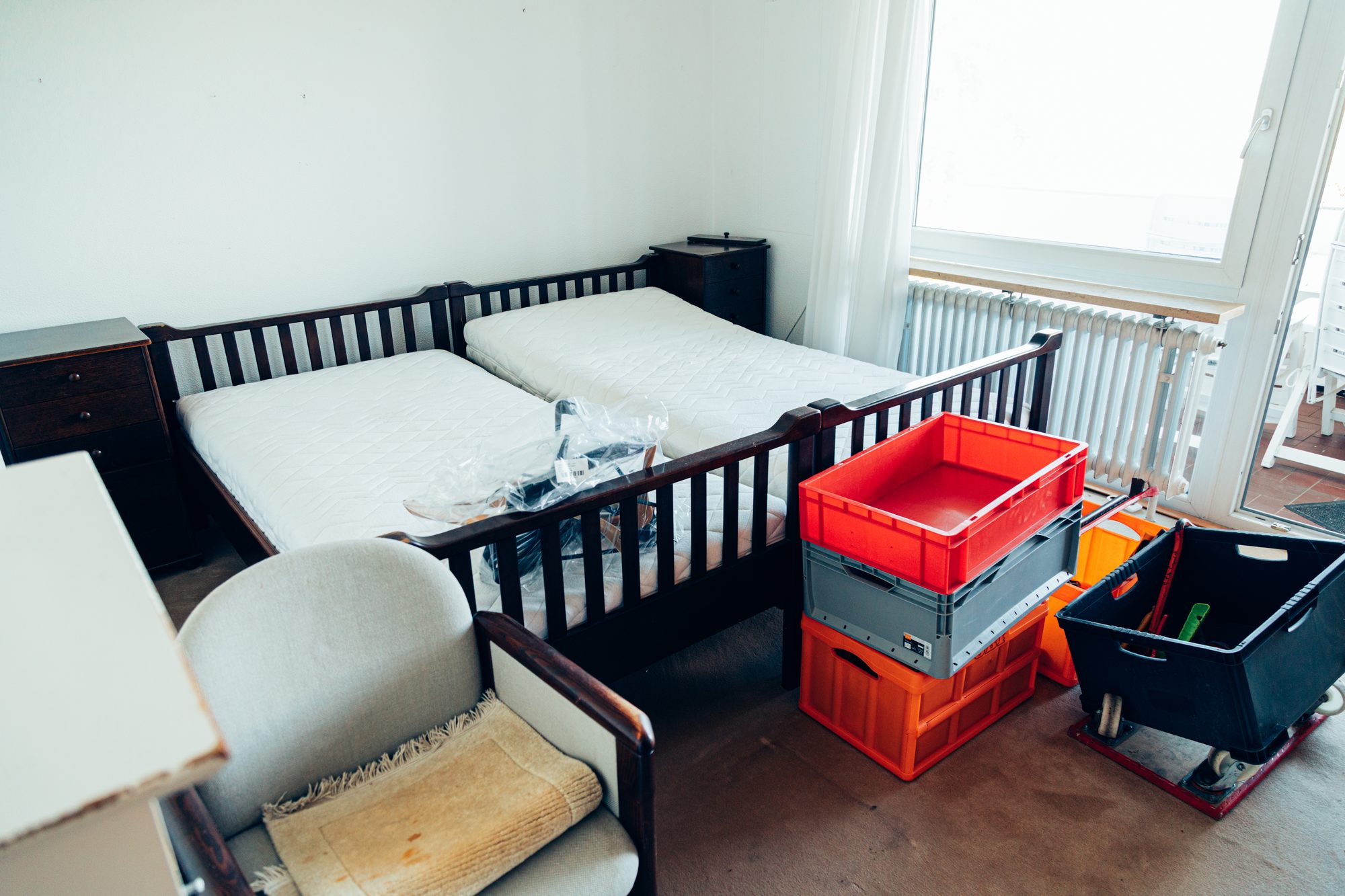 Schlafzimmer mit Doppelbett, Sessel und bereitgestellten Transportkisten vor der Räumung.