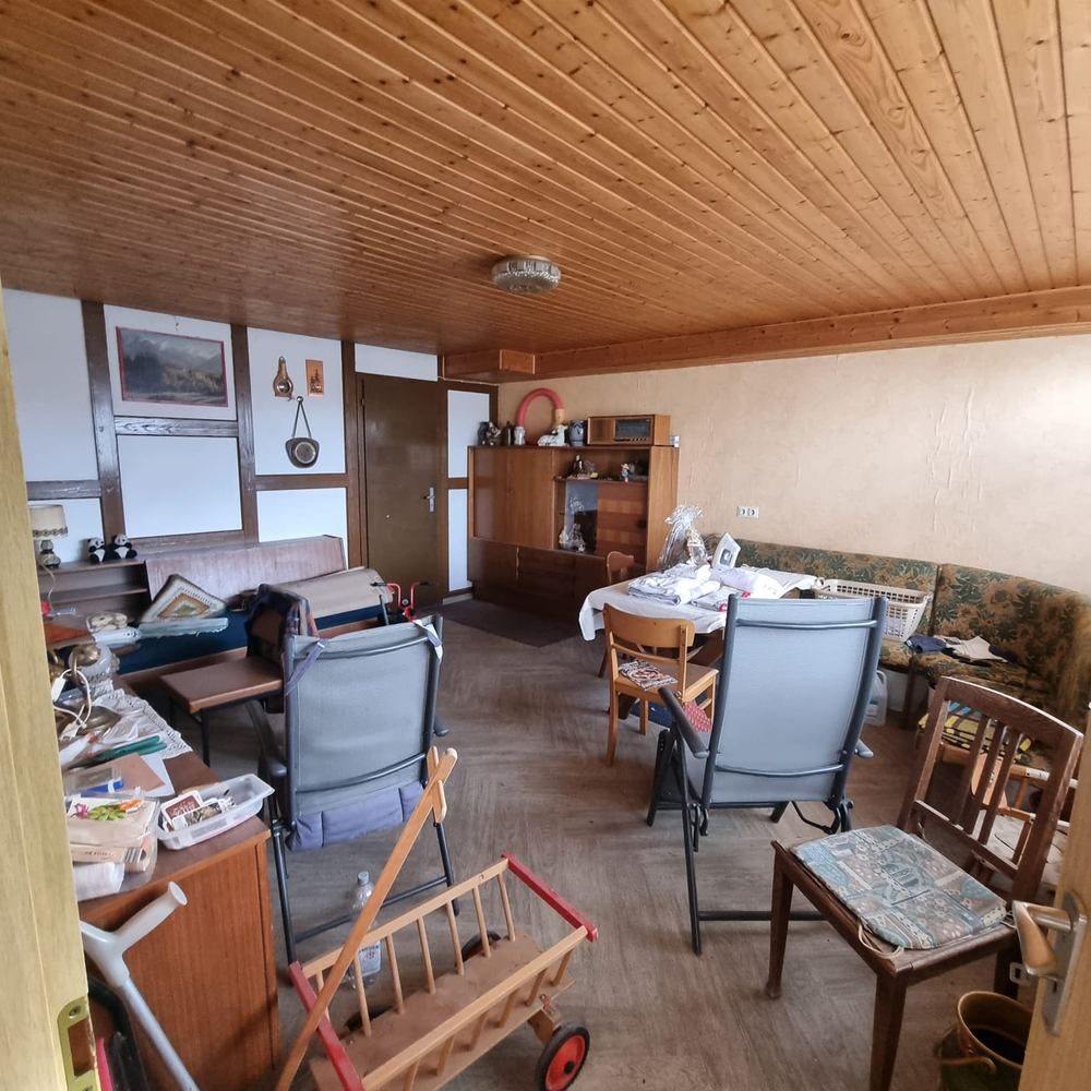 Dicht vollgestelltes Wohnzimmer mit Holzdecke vor einer Haushaltsauflösung.