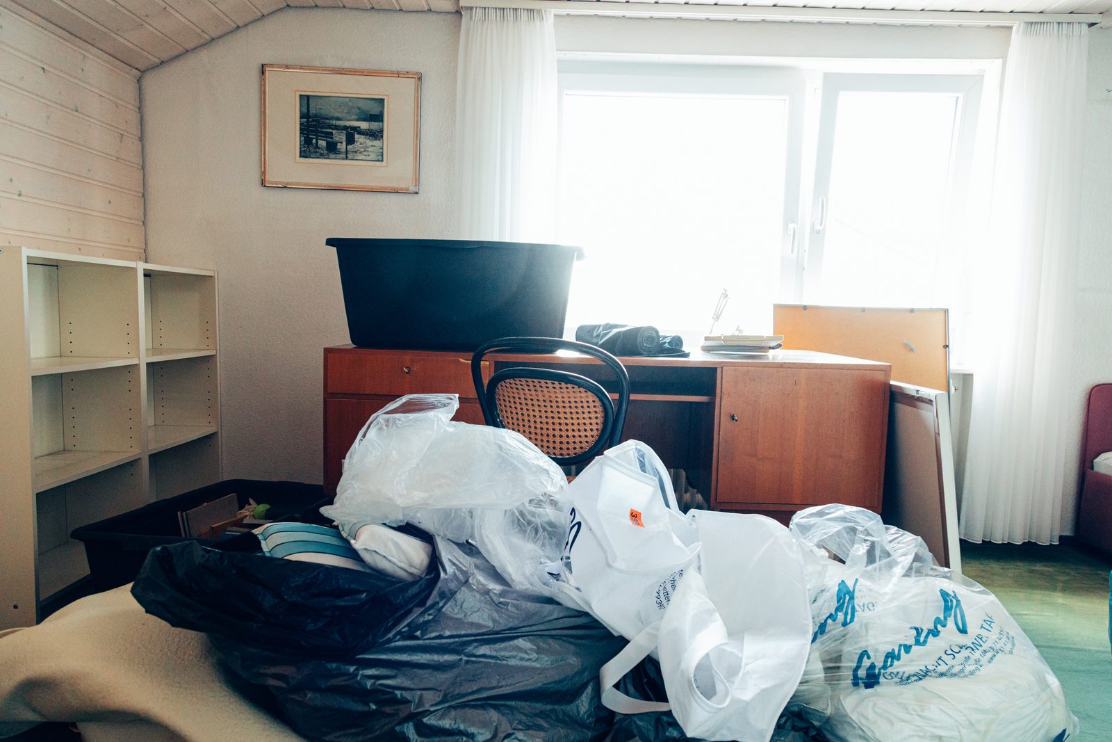 Dachzimmer vor der Räumung, voller Müllsäcke vor Schreibtisch und Regal.