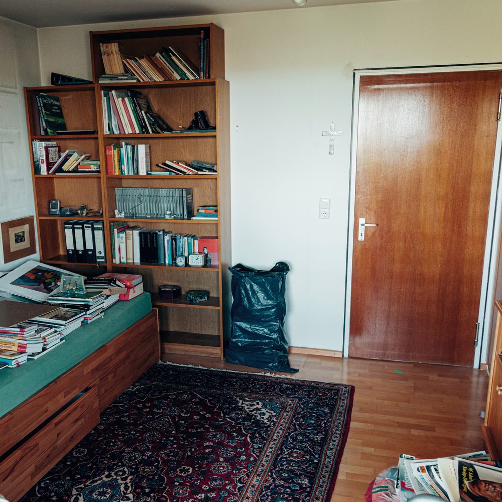 Arbeitszimmer mit Bücherregal, Schlafsofa voller Bücher und Teppich vor der Räumung.