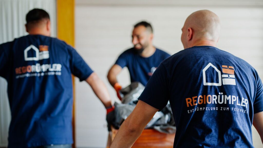 Drei Mitarbeiter in RegioRümpler-Shirts tragen Sperrmüll aus einem Dachzimmer.